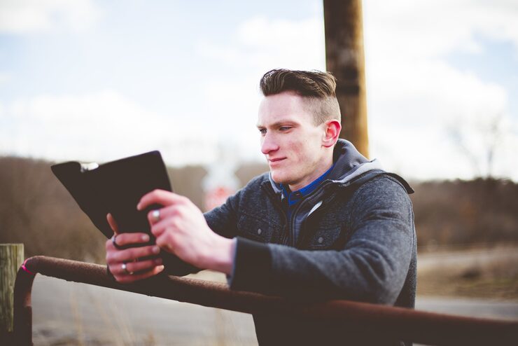 A young man reading the Bible on a digital tablet outdoors, reflecting on God’s Word.